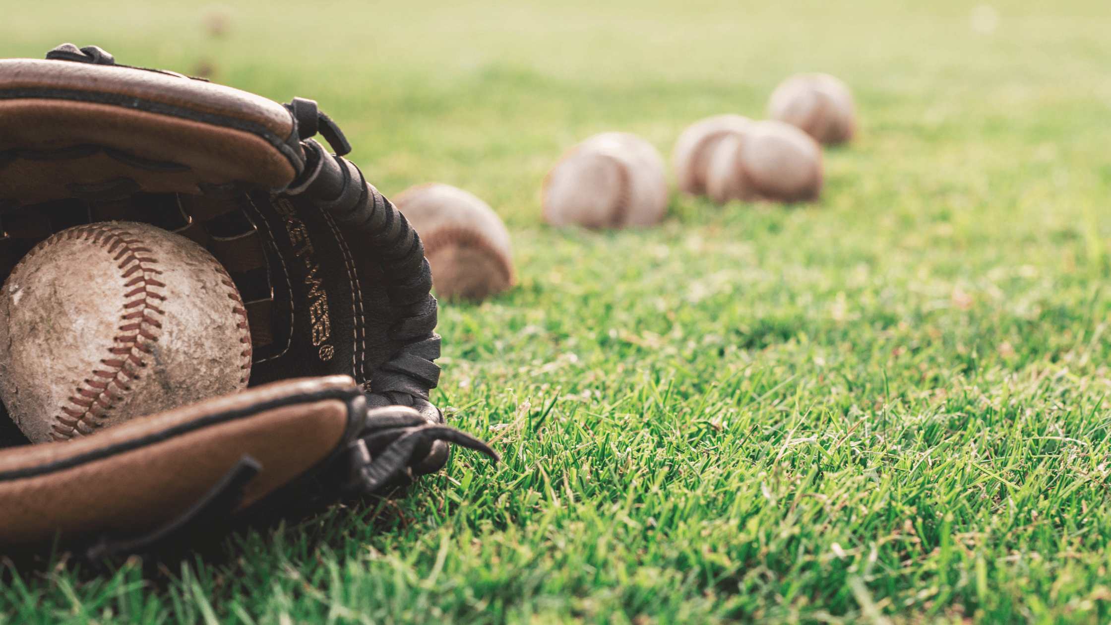 Baseball glove and baseballs on a field.