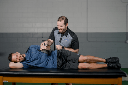 patient on a physical therapy table being worked on by a physical therapist who is working on the patient's arm